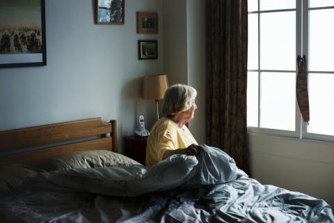 Mujer mayor sentada en la cama mirando por la ventana
